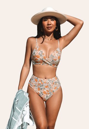 Floral bikini set with orange and cream patterns. Includes a wrap-style bralette and high-waisted bottom. Accompanied by a blue towel.