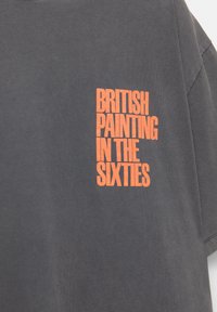 Kullgrå bomulds t-shirt med en iøjnefaldende orange grafisk tekst, der står "BRITISH PAINTING IN THE SIXTIES" på venstre brystområde.