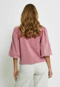 Rosa, strukturerad blus med puffärmar och avslappnad passform. Tyget verkar mjukt med en liten lyster. Kjolslutet är något rundat.