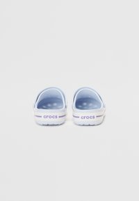 Zoccoli Crocs azzurro chiaro con una texture liscia, apertura posteriore e suola bianca con accento a strisce viola e marchio "crocs".