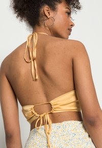 Top halter em satin amarelo com fecho nas costas e corte arredondado. Textura suave com um leve brilho, combinado com uma saia com padrão floral.