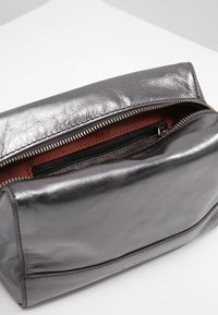 Metaliczna szara skórzana torba z zamkiem błyskawicznym, z wyściełanym wnętrzem w kolorze czerwonobrązowym, prezentująca gładką fakturę i subtelne detale przeszyć.