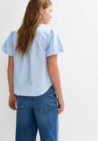 Pale blue striped short-sleeve blouse with puff sleeves, round neckline, and a curved hem, paired with high-waisted blue denim jeans.