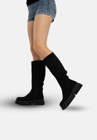 Zwarte suède kniehoge laarzen met een dikke zool en een ritssluiting aan de zijkant, met een gladde textuur en gestroomlijnd ontwerp.