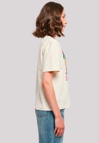 Helle Baumwoll-T-Shirt mit kurzen Ärmeln, das auf der Vorderseite bunte Palmen-Grafiken zeigt. Dazu kombiniert mit hellblauen Jeans.