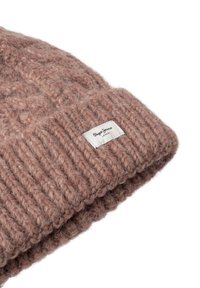 Bonnet tricoté rose en matériau doux avec un design côtelé et une étiquette tissée affichant le nom de la marque et son emplacement.