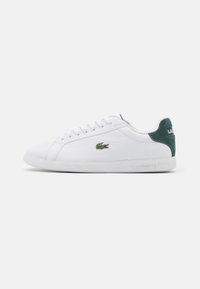 Sneaker bianche basse con il tallone in suede verde, lacci bianchi, parte superiore in pelle texturizzata e logo coccodrillo Lacoste di lato.