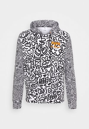 Biała bluza z kapturem z czarnymi abstrakcyjnymi bazgrołami na całej powierzchni oraz małym pomarańczowym logo "Puma x Mr. Doodle" na piersi, przedniej kieszeni i sznurkach.