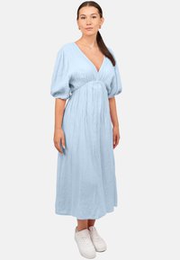 Robe bleu clair, longueur genou, avec un d écolleté en V, des manches bouffantes, un tissu texturé et une taille cintrée ; associée à des baskets blanches.