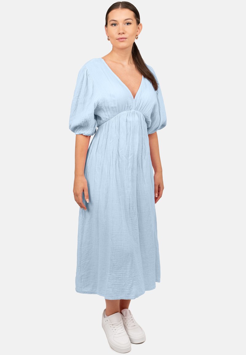 Robe bleu clair, longueur genou, avec un décolleté en V, des manches bouffantes, un tissu texturé et une taille cintrée ; associée à des baskets blanches.