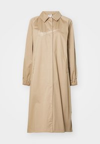 Béžový kabát Nike do poloviny délky s límcem, elastickými manžetami, bočními kapsami a výrazným logem na hrudi. Hladká textura látky.