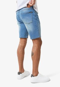 Jeansshorts in hellblau mit einem verblassten Finish. Verfügt über fünf Taschen und ein Lederetikett am Bund. Kombiniert mit weißen Sneakers.
