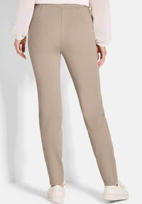 Beige, aansluitende broek van zacht materiaal, met een strak ontwerp zonder zichtbare sluitingen. Gecombineerd met witte sneakers.