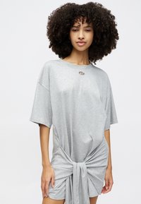 Vestido t-shirt oversized cinza com mangas curtas, apresentando um detalhe de nó na frente e um acabamento prateado na gola. Material de algodão macio.