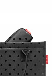 Sac fourre-tout noir à pois, doté d'une texture robuste, avec une petite pochette assortie visible à l'intérieur et une étiquette de marque rouge sur le côté.
