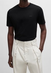 Černé bavlněné tričko s kulatým výstřihem a jemným logem "BOSS". V páru s lehkými béžovými kalhotami s plisováním a texturovaným povrchem.