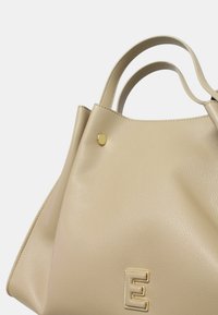 Borsa a mano in pelle beige con doppi manici, bottone dorato e logo "E" in rilievo sulla parte anteriore. Texture liscia, forma strutturata.