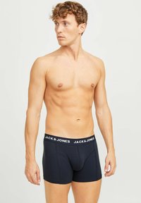 Dunkelblaue Boxershorts mit einem weißen "JACK & JONES"-Logo auf dem elastischen Bund. Glatte Textur, enganliegende Form und modernes Design.