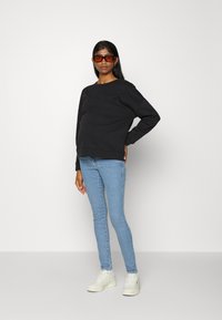 Sweatshirt preto com um corte descontraído, combinado com jeans skinny azul claro e sapatilhas brancas. A modelo usa óculos de sol oversized laranja.