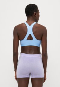 Sostén deportivo de color azul claro con un diseño de espalda nadadora, combinado con pantalones cortos lavanda que cuentan con paneles de malla para mayor transpirabilidad. Textura de tela suave.