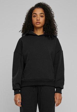 Felpa nera con cappuccio, dal taglio morbido, grande tasca frontale, polsini e orlo a costine, texture morbida, indossata con pantaloni abbinati.