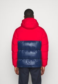 Röd och marinblå vadderad jacka med huva, har en quiltad design, glansig textur i marinblått och matt yta i rött.