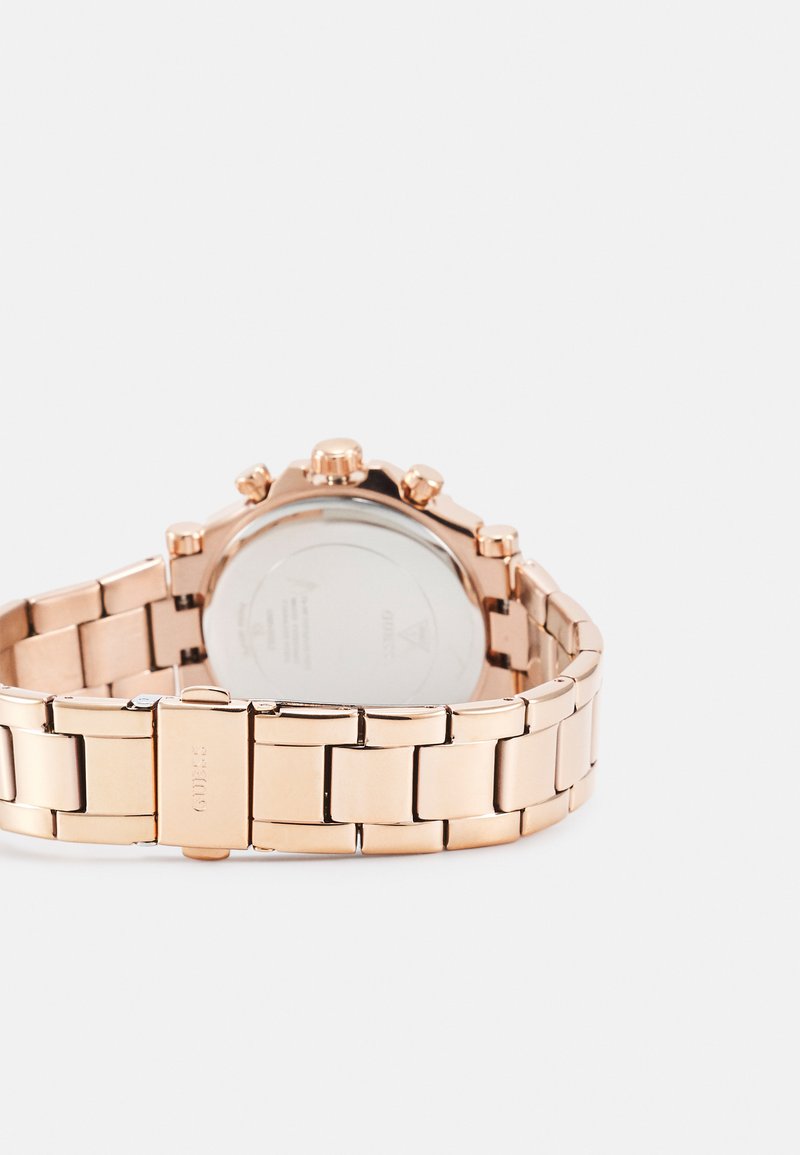 Montre en métal doré rose avec un bracelet à maillon et un boîtier rond. Elle dispose de trois boutons-poussoirs et d'un dos en verre clair montrant le mouvement.