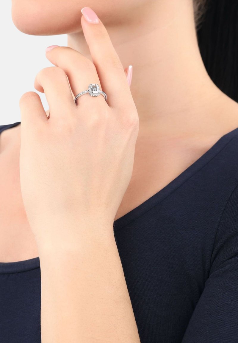 Anello in argento con una pietra centrale taglio smeraldo circondata da diamanti più piccoli, montato su un delicato band con dettagli intricati.