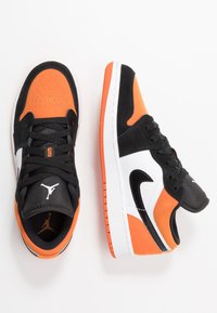 Sneaker basse con tomaia in suede nero e arancione e sintetico, dettagli in pelle bianca e suola in gomma texture.