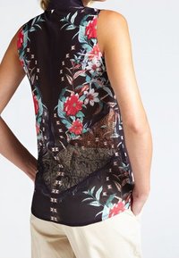 Blusa sin mangas negra con estampado floral en rojo y verde, con acentos de encaje y un diseño trasero texturizado. Acabado de tela suave.