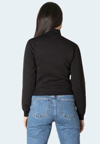 Zwarte cropped sweatshirt met geribde zoom en kraag, gecombineerd met hooggetailleerde blauwe denim jeans met klassieke achterzakken.