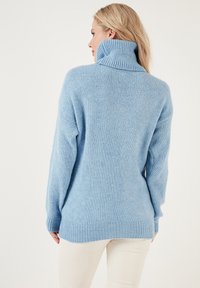 Hellblauer gestrickter Pullover mit hohem Kragen und geripptem Saum. Die Textur wirkt weich und gemütlich und hat einen lässigen, weit geschnittenen Schnitt.