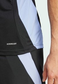 Černé sportovní tričko s světle modrými akcenty, vyrobené z prodyšné tkaniny s texturovanými síťovinovými panely. Obsahuje branding "AEROREADY".