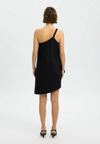 Vestido negro asimétrico con una sola tira trenzada, hecho de una tela suave, que presenta un corte holgado y una longitud por encima de la rodilla.