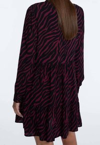Langärmliges Kleid aus leichtem Stoff mit einem schwarz-burgunderfarbenen Zebra-Muster, das einen gestuften Saum und einen lockeren Schnitt aufweist.