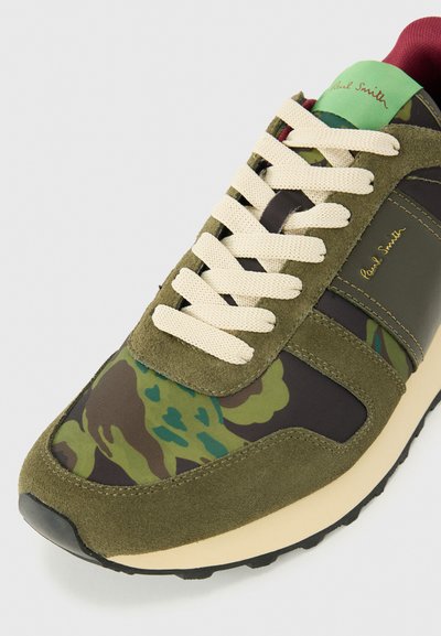 Grüne und braune Camouflage-Sneaker aus Velours- und Textilmaterial, mit cremfarbenen Schnürsenkeln, schwarzem Sohle und dezentem Branding an der Seite.