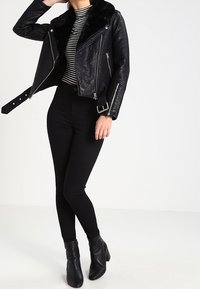 Černá kožená motorkářská bunda s kožichem, zipovými kapsami a stříbrnými doplňky, spárovaná s černými kalhotami s vysokým pasem a kotníkovými botami.