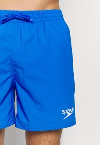 Shorts de bain bleus en tissu léger et résistant à l'eau. Taille élastique avec cordon de serrage. Logo blanc "Speedo" sur le bas devant.