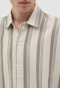 Camicia abbottonata con tessuto testurizzato a righe verticali in beige, verde oliva e blu navy. Collo classico e bottoni frontali.
