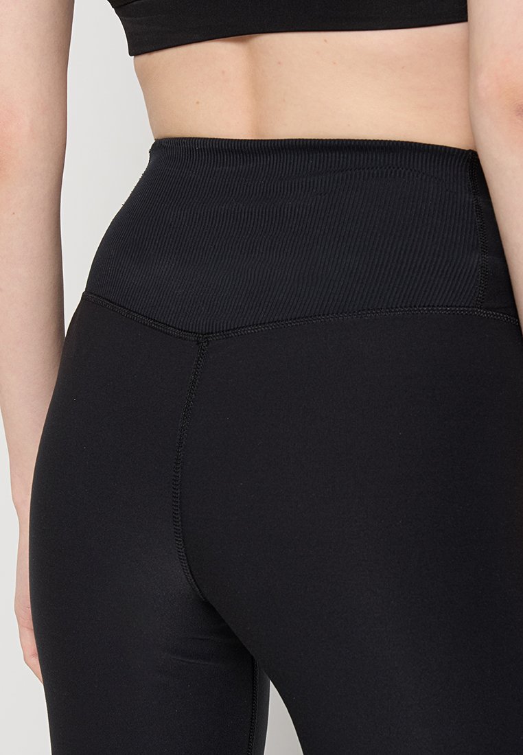 Ingrandimento di una persona che indossa leggings neri a vita alta a costine e un crop top nero, mostrando la parte bassa della schiena e l'area della vita.