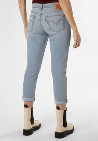 Jasnoniebieskie dżinsy o zwężanym kroju, z podwiniętymi mankietami i pojedynczymi tylnymi kieszeniami z naszywką logo Levi's. Masywne beżowe botki z czarnymi akcentami.