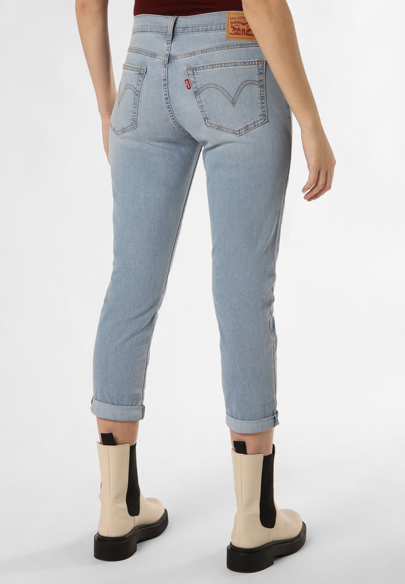 Jeans de mezclilla de color azul claro con un corte ceñido, puños enrollados y un solo bolsillo trasero con el parche del logo de Levi's. Botas beige gruesas con detalles en negro.