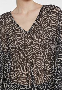 Top trasparente e plissettato con scollatura a V. È stampato in nero e beige con motivi astratti, evidenziando una texture leggera e fluida.