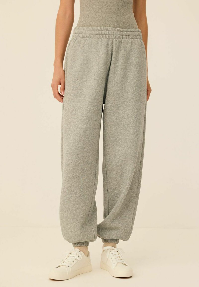 Jasnoszare dresy wykonane z miękkiego, teksturowanego materiału, z elastycznym paskiem w talii i ściągaczami przy mankietach, w połączeniu z białymi butami sportowymi.