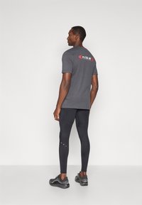 Γκρι μπλούζα με κόκκινη και λευκή σήμανση Nike στην πλάτη, συνδυασμένη με μαύρα κολάν και γκρι αθλητικά παπούτσια. Λείο ύφασμα, εφαρμοστό σχέδιο.