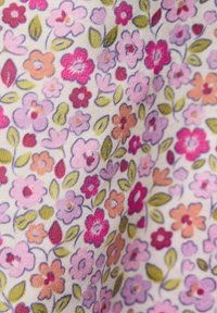 Virágmintás textil, amelyen kis rózsaszín, lila és narancssárga virágok, valamint zöld levelek láthatók világos háttéren.
