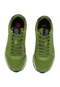 Un paio di scarpe da corsa verdi con lacci, solette interne nere contrassegnate "R" e "L", e etichette sulla linguetta che leggono "CORRI PIÙ VELOCE DI QUANTO PUOI."