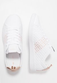 Białe sneakersy Lacoste z wytłoczonym napisem i różowozłotymi akcentami, pokazane z widoku z góry i z boku na białym tle.
