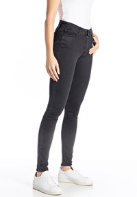 Mustat kapeat farkut, jotka on valmistettu sileästä denimistä, varustettu vetoketjulla ja napilla kiinnitettäväksi, sekä etupussit yksityiskohtina.