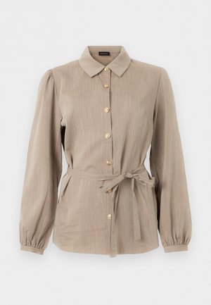 Μπεζ πουκάμισο με μακριά μανίκια και κουμπιά, γιακά, ελαφρώς φουσκωτά μανίκια και υφασμάτινη ζώνη δεμένη στη μέση.